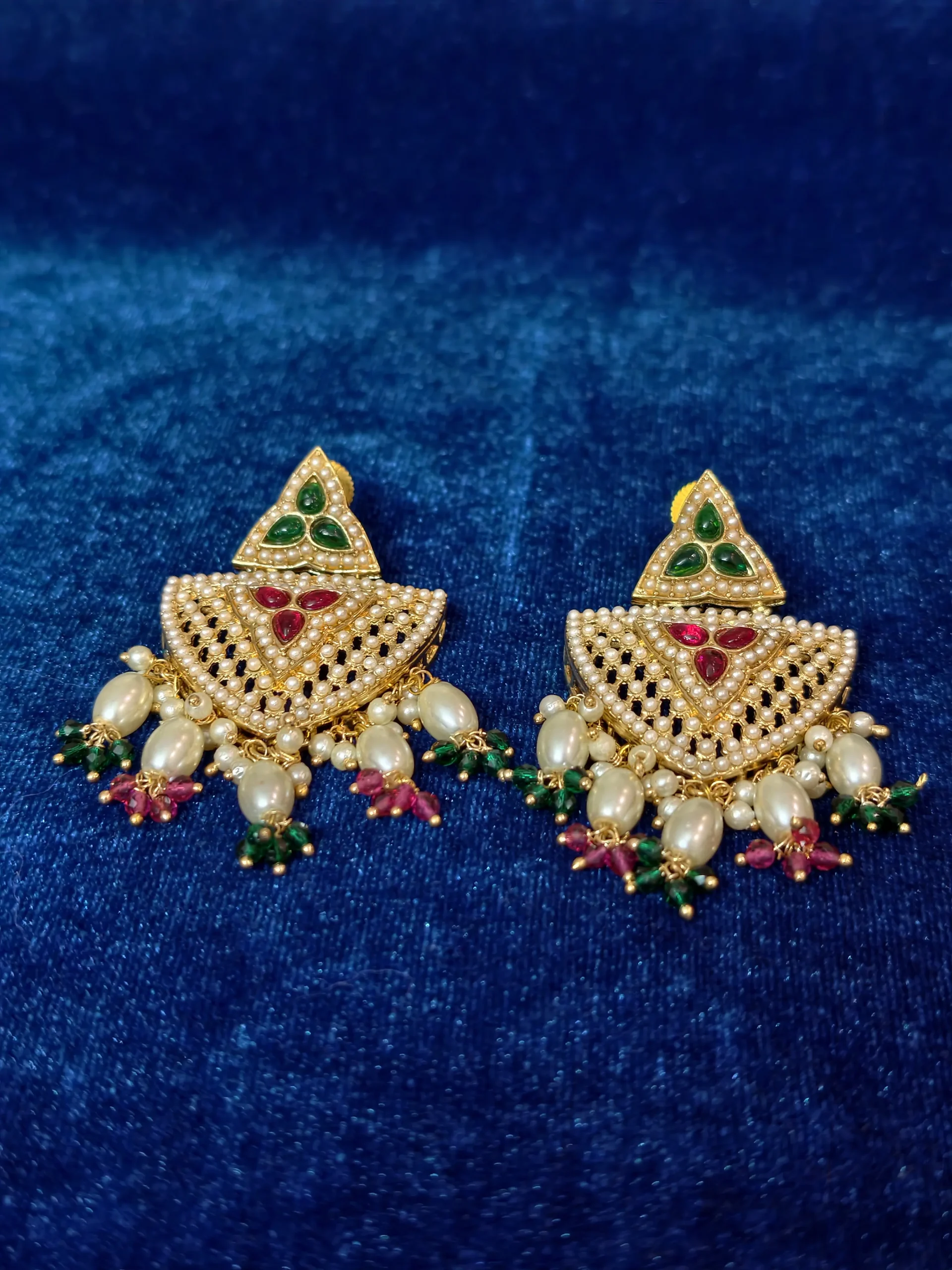 A distinctive multi-strand pearl necklace set featuring a shield-shaped pendant, maroon and green stone accents, and matching statement earrings
